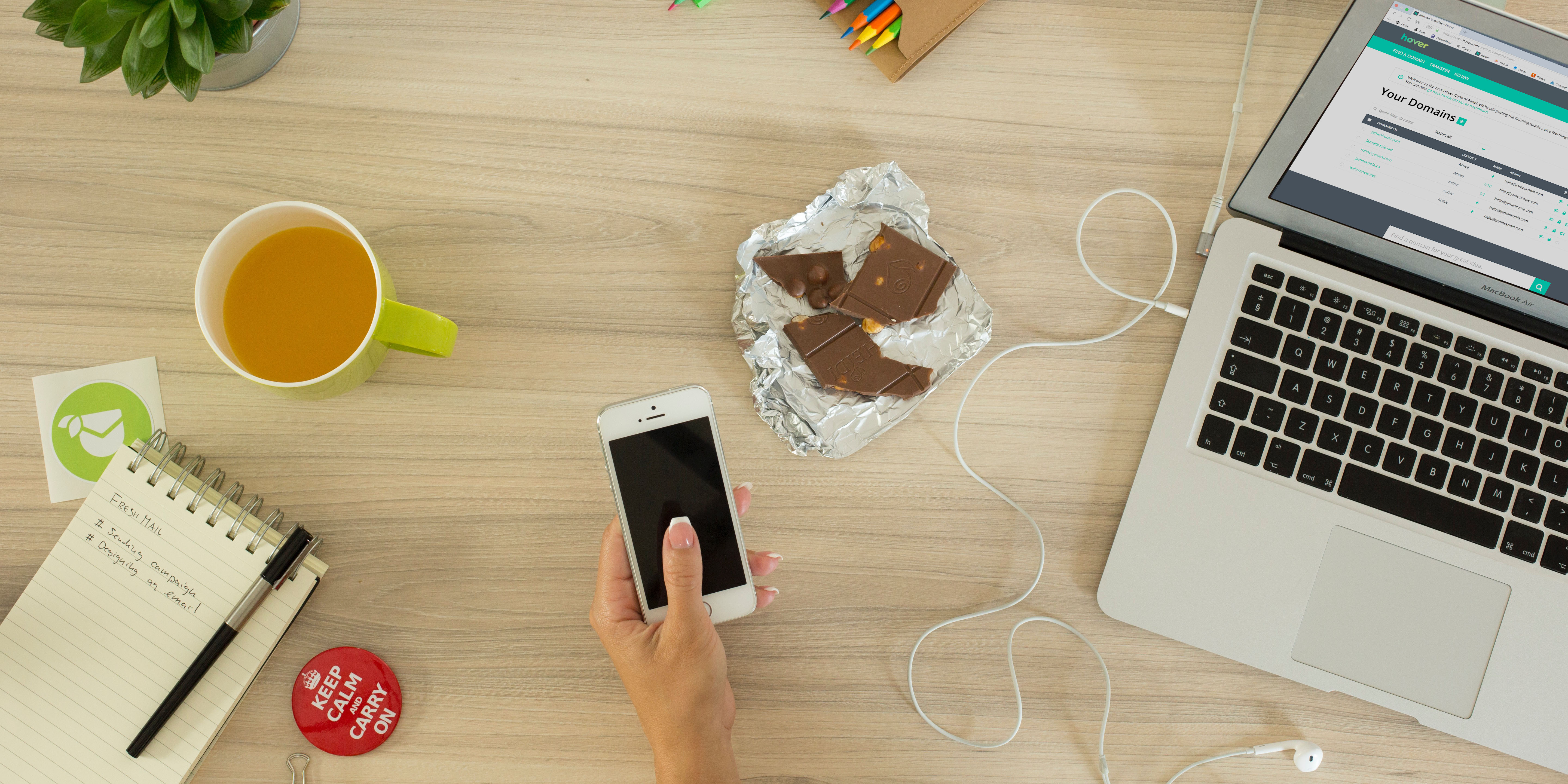 A person using a phone and a laptop on a cluttered desk. And there's chocolate.