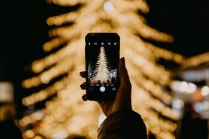 Person taking a photo of a holiday tree with lights covering it