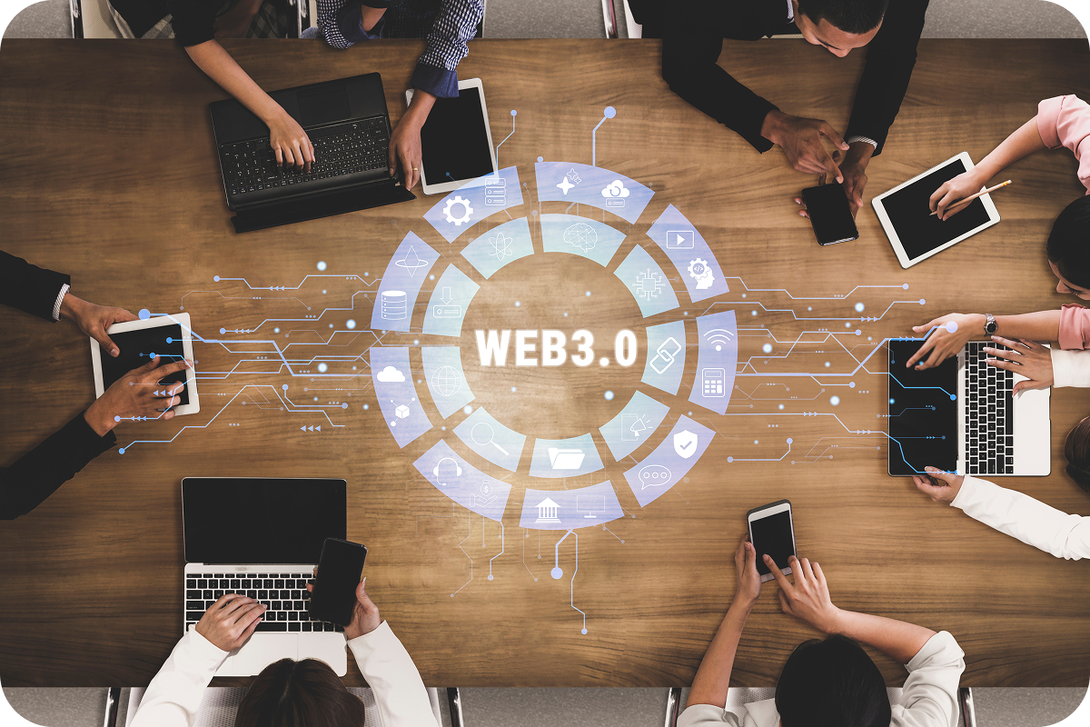 View from above of several people working at a desk, suing laptops and phones. A Web3 graphic in the middle of the table.